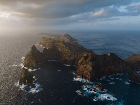 Aerial view of Ponta de Sao Lourenco peninsula with dramatic volcanic cliffs and dark ocean waves under a cloudy sky in Canical, Madeira, Portugal.