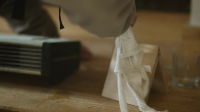 Hands meticulously clean a wooden frame with a white cloth. This scene highlights the careful preparation of a wood object.