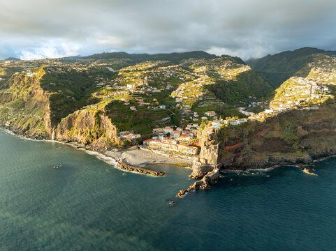 Aerial view of the coastal village of Ponta do Sol nestled between steep cliffs and terraced hills under a cloudy sky Ponta do Sol, Madeira, Portugal.