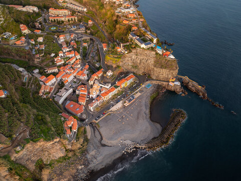Aerial view of the coastal town of Ponta do Sol with colorful buildings, a pebble beach, and a stone breakwater along the Atlantic coast in Ponta do Sol, Madeira, Portugal.