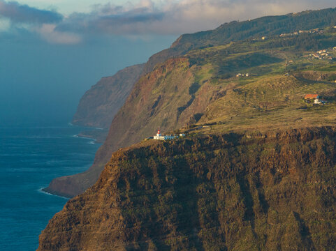 Aerial view of the Ponta do Pargo Lighthouse perched on high rocky cliffs overlooking the Atlantic Ocean under a soft sunset sky in Ponta do Pargo, Madeira, Portugal.