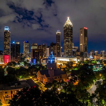 Illuminated cityscape at dusk, showcasing numerous skyscrapers. Night sky is a deep blue and light pollution glows