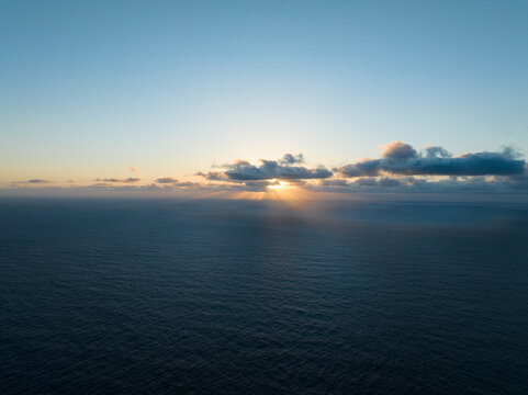Aerial view of sunbeams breaking through clouds over the vast Atlantic Ocean during sunset from Miradouro do Ponta da Ladeira in Porto Moniz, Madeira, Portugal.