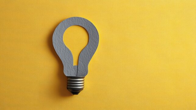 Light bulb shape cutout made from gray paper on a vibrant yellow background, symbolizing creativity and innovation in design and ideas