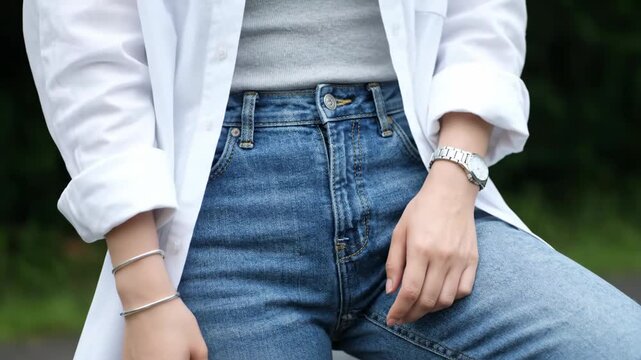 Stylish woman poses in blue jeans and a white shirt outdoors