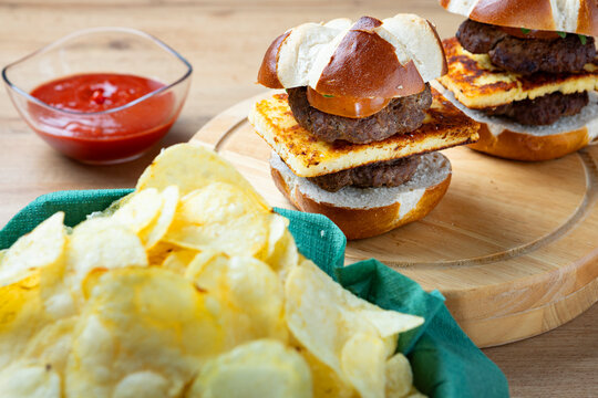 Homemade mini burgers sliders served on wooden board with potato chips and ketchup, shallow depth of field food composition, casual snack or street food concept.