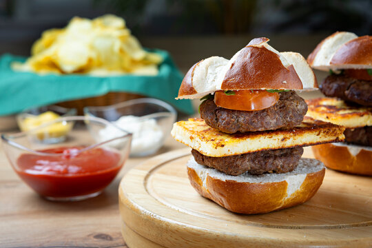 Homemade mini burger sliders with grilled cheese and beef patties on wooden board, served with chips and sauces, appetizing food styling for fast food or casual dining concept.
