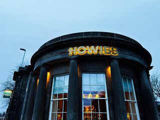Obraz premium Howies restaurant front at dusk in Edinburgh, Scotland showing a historic round stone building with illuminated sign and classical columns