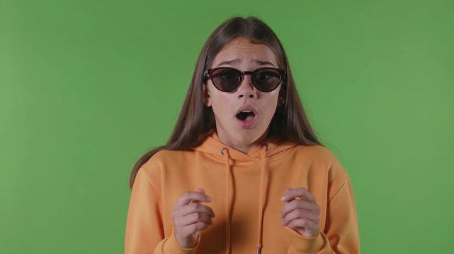 Surprised woman wearing sunglasses reacting with shock in front of green screen background expressive studio portrait for chroma key video production