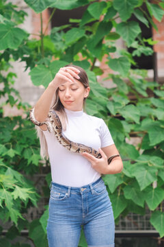 Young woman holding a python snake in an abandoned urban environment, wild concept