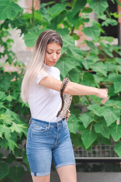 Young woman holding a python snake in an abandoned urban environment, wild concept