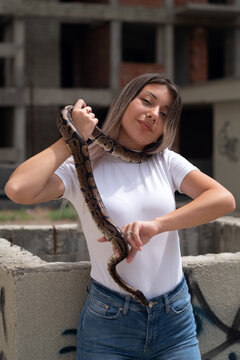 Young woman holding a python snake  in an abandoned urban environment, wild animal concept