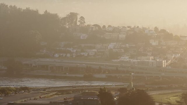Hazy morning light illuminating the residential hills and highway traffic in Berkeley, California, with a marina and the San Francisco Bay visible in the foreground