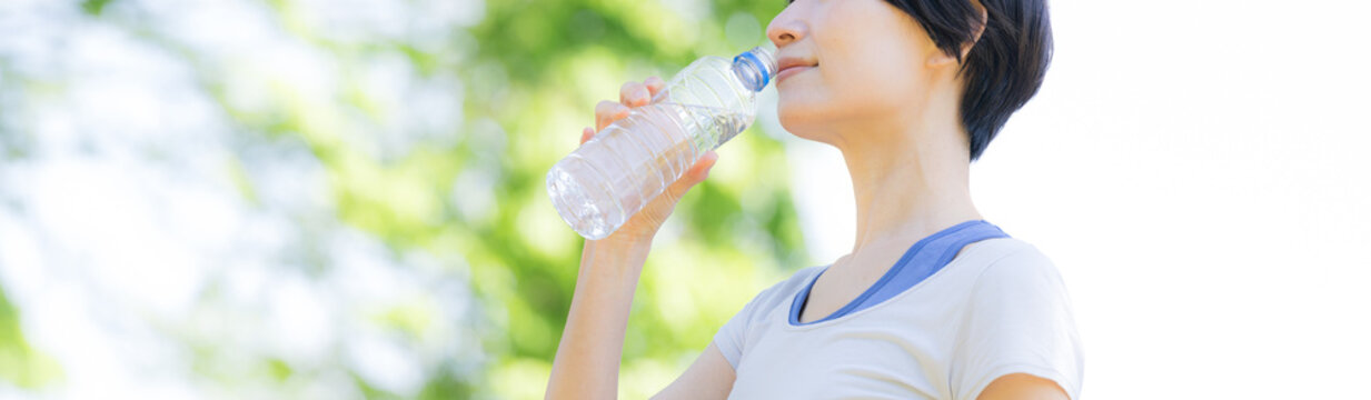 新緑の屋外で水分補給をする女性の横顔ポートレート　ウォーキングやランニングの運動やスポーツの間にペットボトルの水を飲むクローズアップ　春夏の半袖バナー顔無し