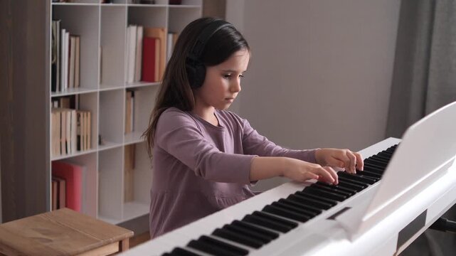 Young girl wearing headphones practices on a digital piano at home, focused on her music lesson and developing skill with hands on the keys in a quiet, enjoyable moment