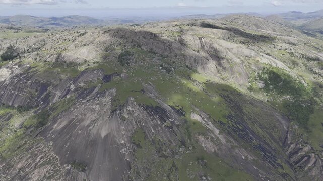 Drone orbits to the right in ultra wide shot of the western face of the rocky summit under cloud cover on a sunny day at Sibebe Rock near Mbabane, Eswatini
