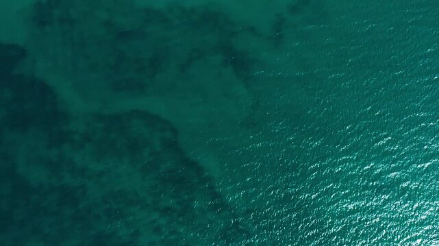 The rich teal sea of Midnight Pass shimmers under sunlight, revealing subtle underwater patterns. Suitable for nature documentaries or environmental content.