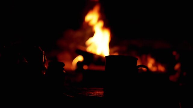 Cozy scene of a mug by a campfire at night. The warm glow of the flames provides a peaceful atmosphere, perfect for camping, relaxation, or simple living.