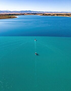 Aerial view of two paddle boarders crossing a turquoise reservoir lake in a desert landscape, summer travel adventure, active leisure and recreation