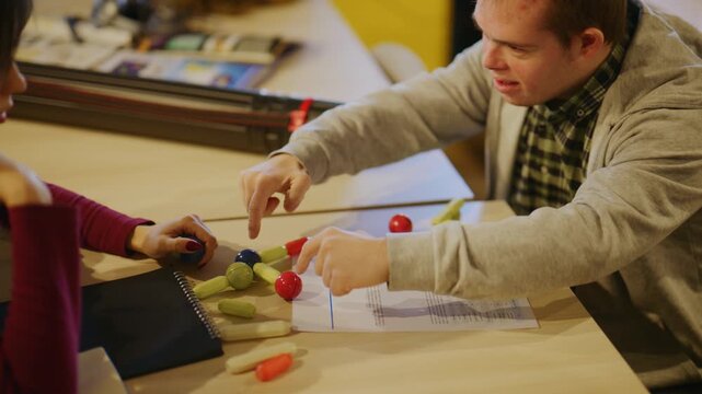 A student with Down syndrome and a partner collaborate on a developmental learning activity. They engage with colorful blocks, sharing a high-five for their successful progress.