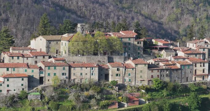 Aerial view of the historic stone village of Trappola with red-tiled roofs and a church tower nestled on a lush green hillside in Trappola, Tuscany, Italy.