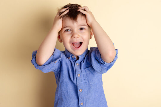Boy of three years in a blue shirt on a yellow background. Emotional portrait.