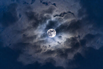 Fototapeta premium A full moon shines through a dramatic, cloudy night sky.
