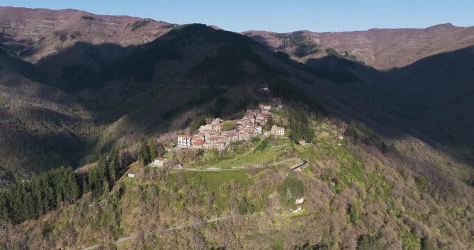 Aerial view of the historic stone village of Trappola nestled on a mountain ridge surrounded by dense forests and rolling hills in Trappola, Tuscany, Italy.