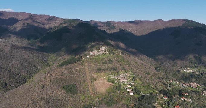 Aerial view of the small stone houses of Trappola village perched on a green ridge surrounded by forested mountains under a clear sky Trappola, Tuscany, Italy.