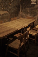 Cozy, rustic cafe with a sturdy wooden table and empty matching chairs in warm, dim lighting. © Aliioss