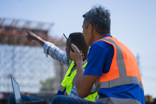 civil engineers using laptop and walkie talkie at construction site