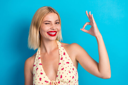 Smiling young woman in a floral halter top winks at the camera against a blue background showcasing playful summer style