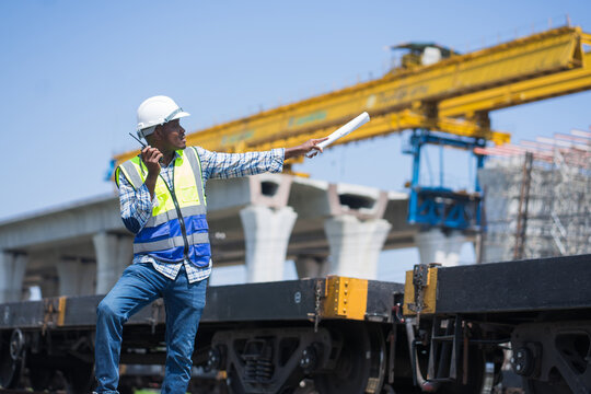 A civil engineer using a walkie-talkie and pointing at a large construction site