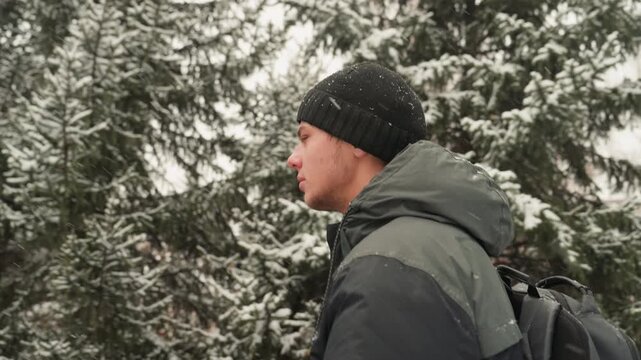 Profile of white man hiking through snowcovered pine forest, wearing knit beanie, green parka and backpack, slow contemplative stride, soft snowfall and muted winter light, cozy outdoors mood, mindful