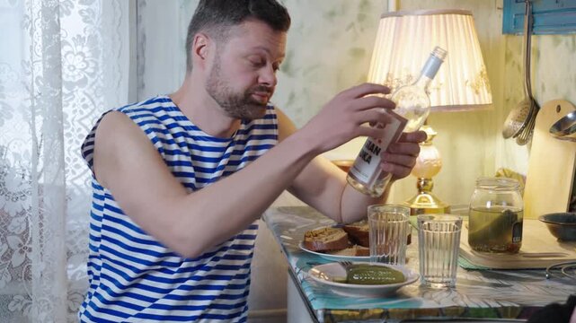 Man alcoholic wearing striped t-shirt drinking Russian vodka with friend sitting on the kitchen with 1990 style interior