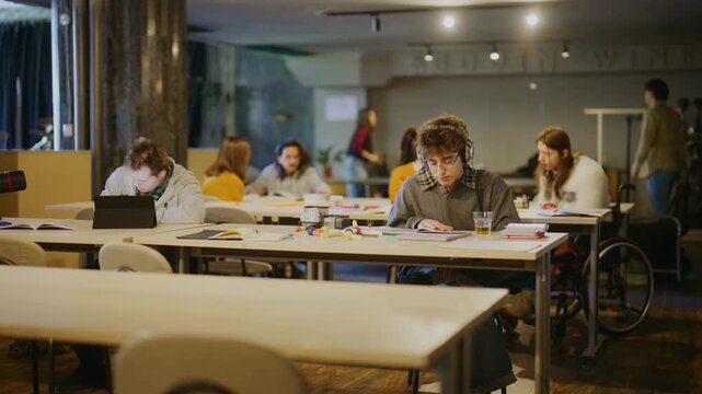 Students are engaged in focused learning activities within a modern inclusive classroom. Young adults are seen studying, reading, and using tablets, highlighting an inclusive educational setting.