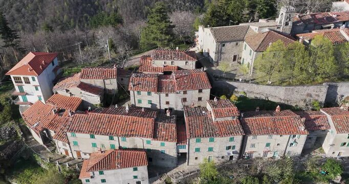 Aerial view of the historic stone houses and terracotta roofs of Trappola nestled in the lush green hills of the Pratomagno mountain range in Trappola, Tuscany, Italy.