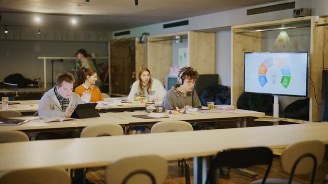 Young students are actively engaged in learning activities within a modern classroom. They are utilizing technology and traditional methods to study and collaborate.