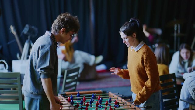 Two young students engage in a friendly game of foosball, showcasing their playful competition and enjoyment. Young people are seen enjoying leisure activities in a casual and social environment.