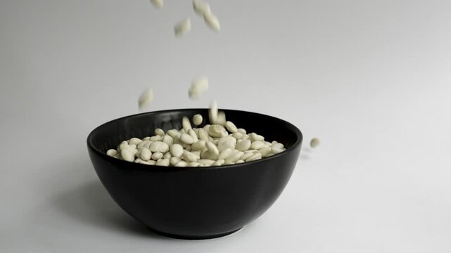 White_beans_filling_black_bowl_white_background_4k_10bit_120fps