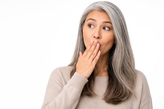 Surprised mature woman covering mouth with hand looking aside isolated on light background