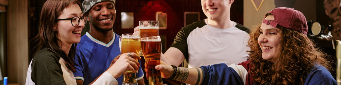 Multiethnic young adults clinking beer glasses in bar, celebrating friendship and social gathering. Ideal for nightlife marketing, youth lifestyle campaigns, community promotion