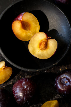 Plums in a black wood bowl on a dark surface 