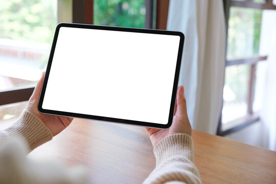 Mockup image of a woman holding digital tablet with blank white desktop screen at home