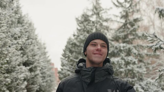 Man pauses quietly. Snowy park with reflective man. Urban park scene with man enjoying winter snowfall. Serene winter setting showing man resting among snowcovered pines with urban background