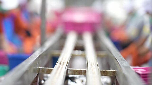 an empty automated conveyor belt system in a modern factory production line with blurred industrial workers in background.