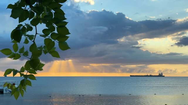 Two large ships move across the ocean as the sun sets on the horizon. Clouds hang above the water and the light reflects on the waves. This moment shows a vast ocean view.