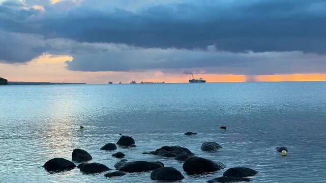 Two large ships move across the ocean as the sun sets on the horizon. Clouds hang above the water and the light reflects on the waves. This moment shows a vast ocean view.