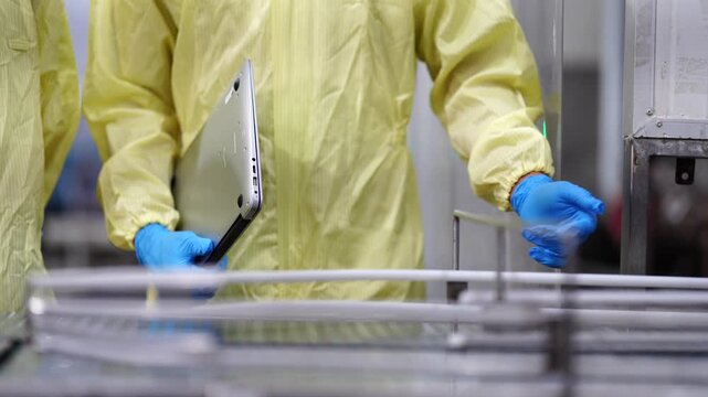 A quality assurance specialist in a yellow protective suit recording data while auditing an automated canning production line in a modern food manufacturing plant.