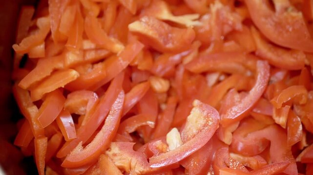 Freshly sliced red bell peppers fill the frame in a detailed close-up highlighting their juicy texture. Concept of healthy vegetarian cooking and preparing fresh organic ingredients.